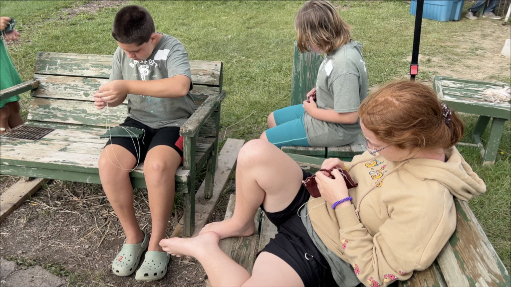 Children sitting on a bench sewing leather pouches
